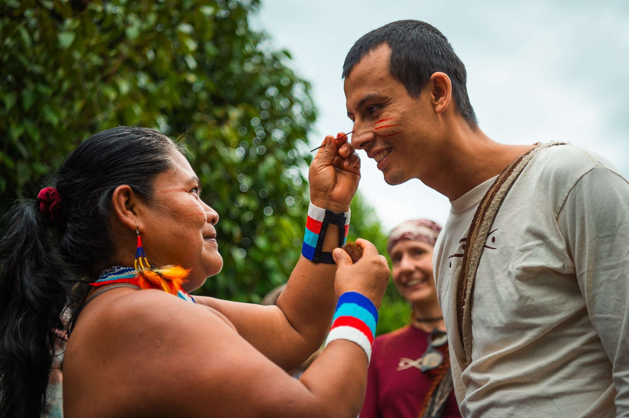 A female Shuar elder applies achiote paint to a man's face as a protection and welcome ritual.